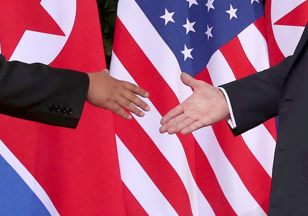 Kim Jong-un e Donald Trump se cumprimentam em hotel em Singapura. Ao fundo, bandeiras da Coreia do Norte e dos Estados Unidos — Foto: Reuters/Jonathan Ernst