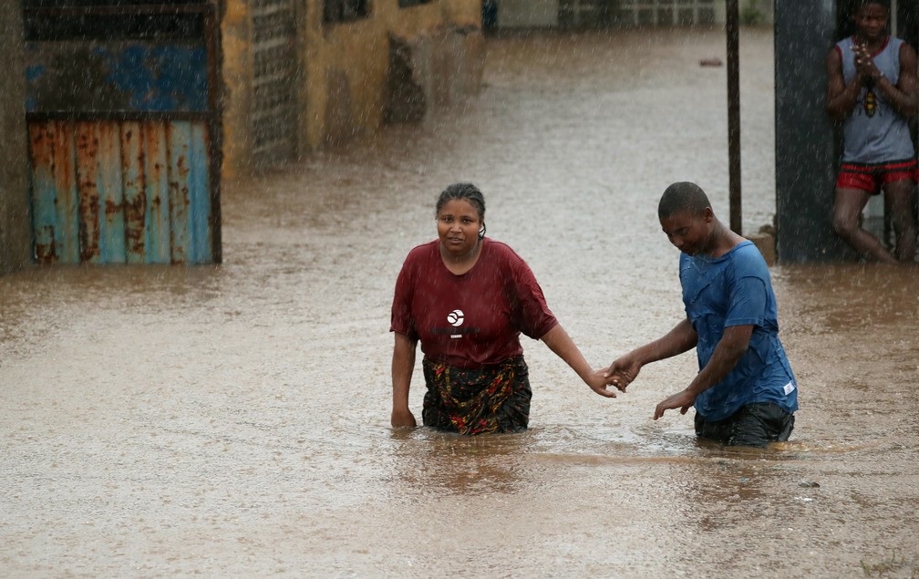 Homem ajuda uma mulher através de uma vizinhança inundada depois da passagem do ciclone Kenneth, na cidade de Pemba, em Moçambique, neste domingo (28). — Foto: Mike Hutchings/Reuters