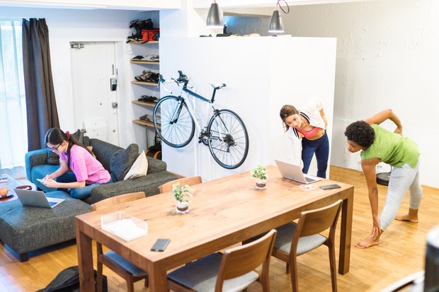 A young woman is working on a laptop while her roommates are doing yoga in their shared apartment. (Foto: Getty Images)