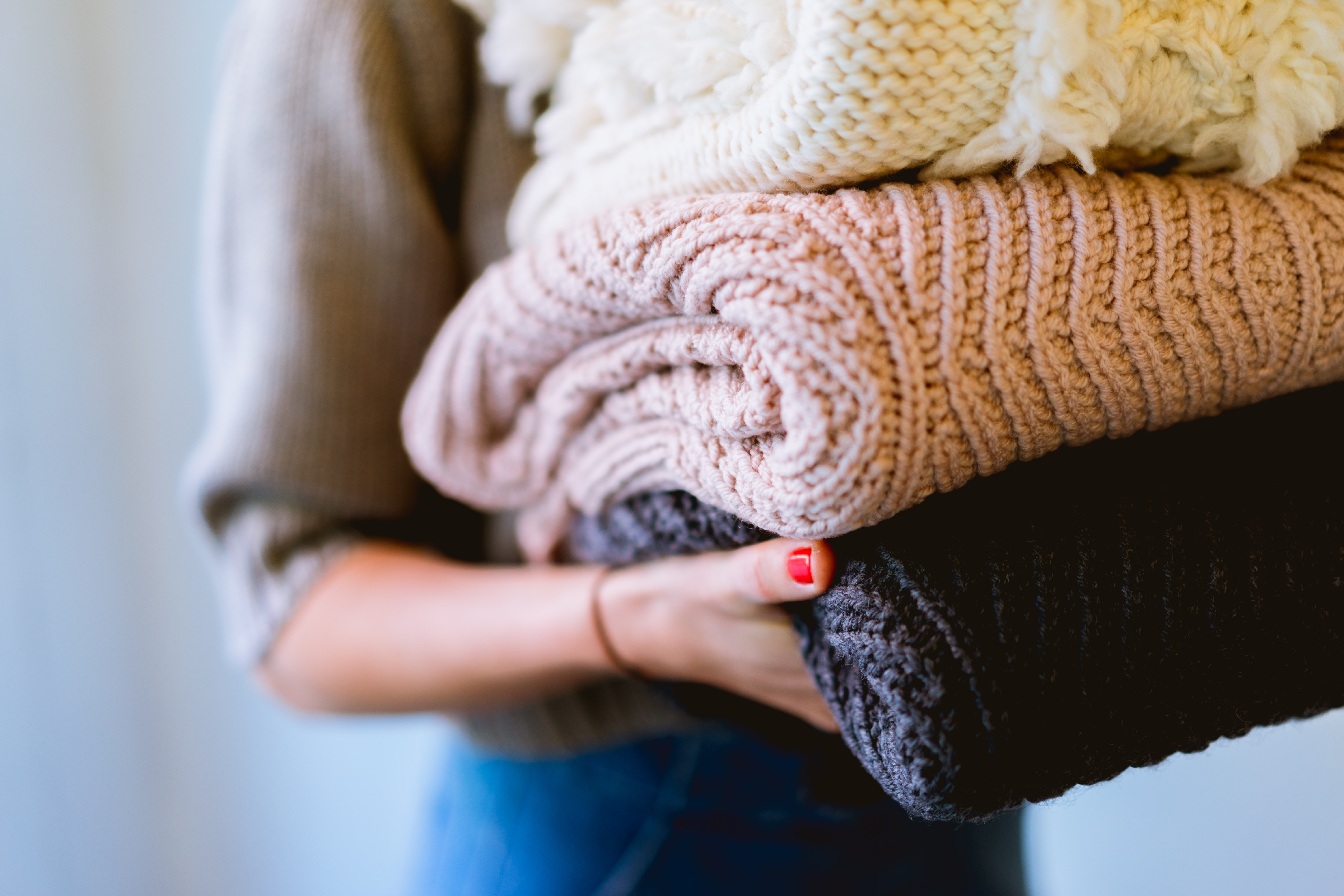  14 truques incríveis para deixar sua casa mais organizada. Acima: mulher segura três suéteres de lã dobrados (Foto: Dan Gold//Unsplash)
