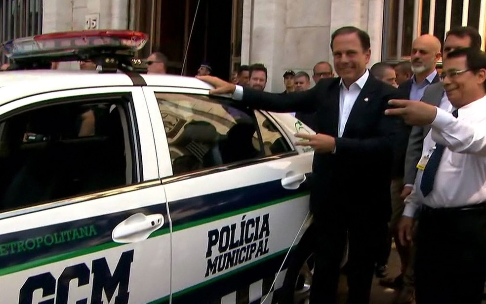O prefeito João Doria posa ao lado de carro da GCM com o nome Polícia Municipal (Foto: TV Globo/Reprodução)
