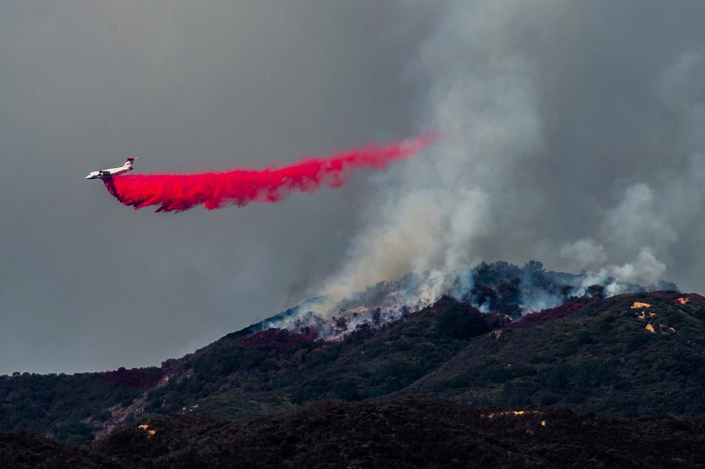 Avião deixa um rastro vermelho no céu despejando retardador de fogo no combate a incêndio na Floresta Nacional Cleveland, perto de Corona, na Califórnia (EUA) (Foto: Watchara Phomicinda/The Orange County Register via AP)