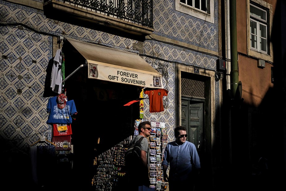 Turistas caminham em frente à loja de lembranças em Lisboa