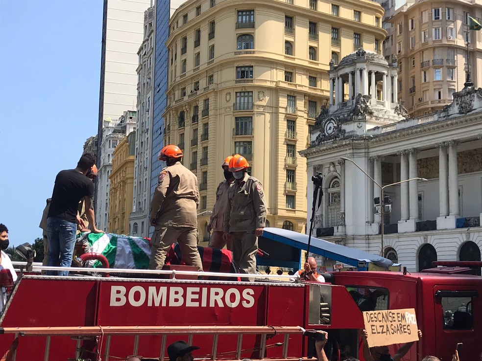 Corpo de Elza Soares é levado em cima do carro dos bombeiros, coberto por uma bandeira da Mocidade — Foto: Matheus Rodrigues/g1