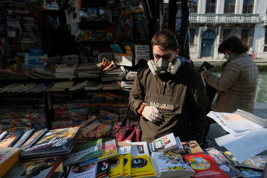 Homem com máscara e luvas floreia livros em banca reaberta de Veneza, na Itália, na terça-feira (14) — Foto: Manuel Silvestri/Reuters