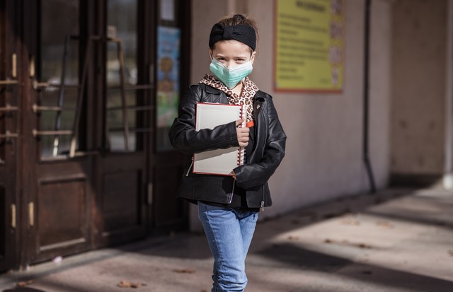 School girl with books in her hands wearing surgical mask on her face (Foto: Getty Images)