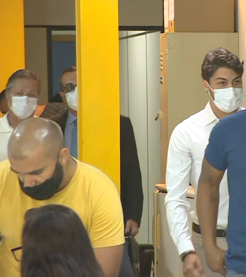 Marcinho (E), de máscara, chega para prestar depoimento — Foto: Reprodução/TV Globo