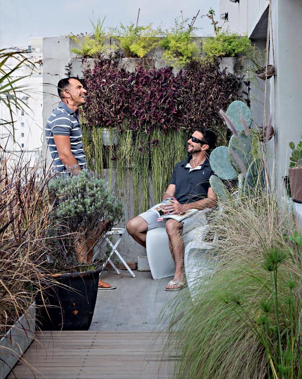 Terraço íntimo | Ronaldo e Hubert, sentado na cadeira Panton, da Artesian, junto à parede verde feita de blocos de concreto da Leroy Merlin (Foto: Evelyn Müller/Divulgação)