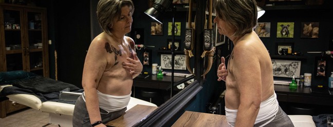  Jacqueline van Schaik, sobrevivente de câncer de mama, se olha no espelho depois de terminar a tatuagem em torno das cicatrizes de mastectomia — Foto: Simon Wohlfahrt/AFP