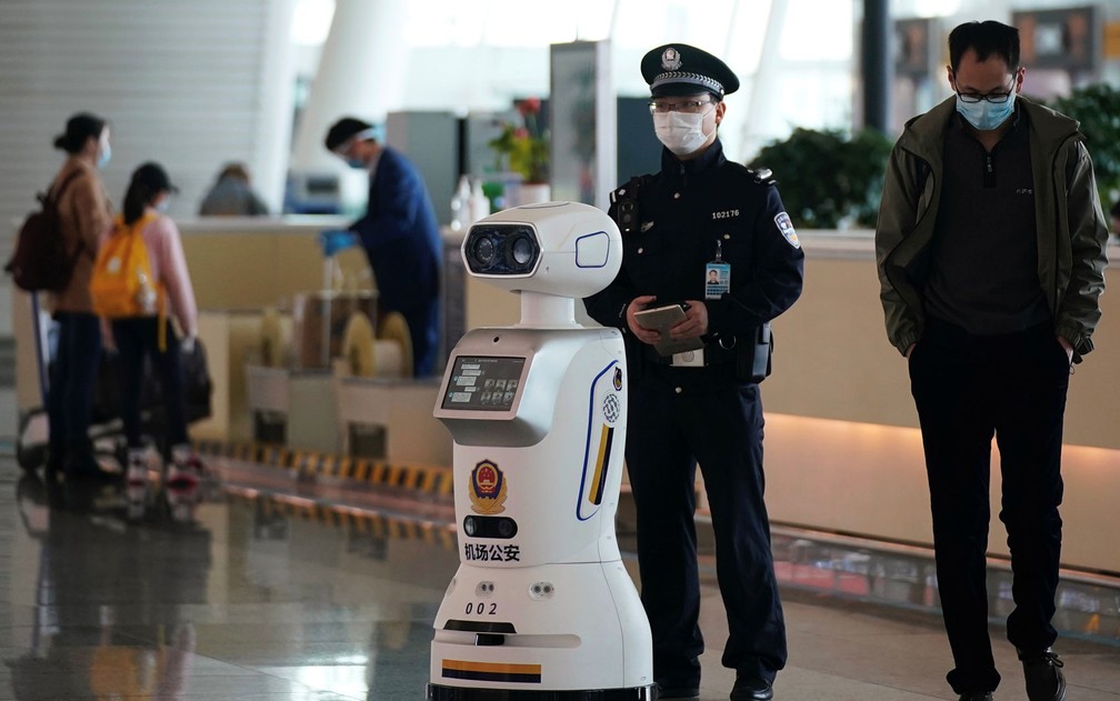  Policial é visto ao lado de robô da polícia no Aeroporto Internacional Tianhe, em Wuhan, após o fim das restrições de viagem na província de Hubei, na China, na quarta-feira (8) — Foto: Reuters/Aly Song 