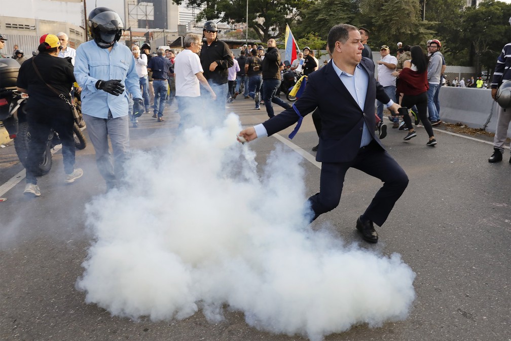 Homem contrário ao governo de Nicolás Maduro atira de volta uma bomba de gás lacrimogêneo atirada por militares da base aérea 'La Carlota', diante da qual um grupo se concentra em Caracas — Foto: Ariana Cubillos/AP