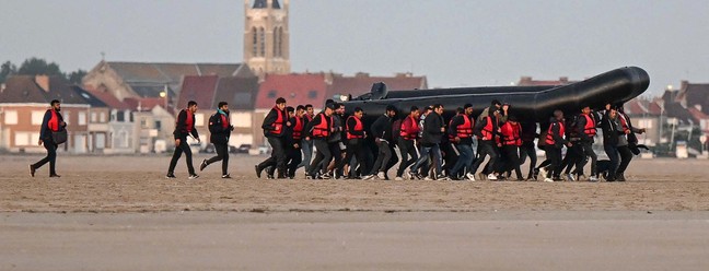 Cerca de quarenta migrantes, de várias origens, carregam um bote inflável em direção à água antes de tentarem cruzar ilegalmente o Canal da Mancha para a Grã-Bretanha, perto da cidade de Gravelines, no norte da França  — Foto: DENIS CHARLET / AFP