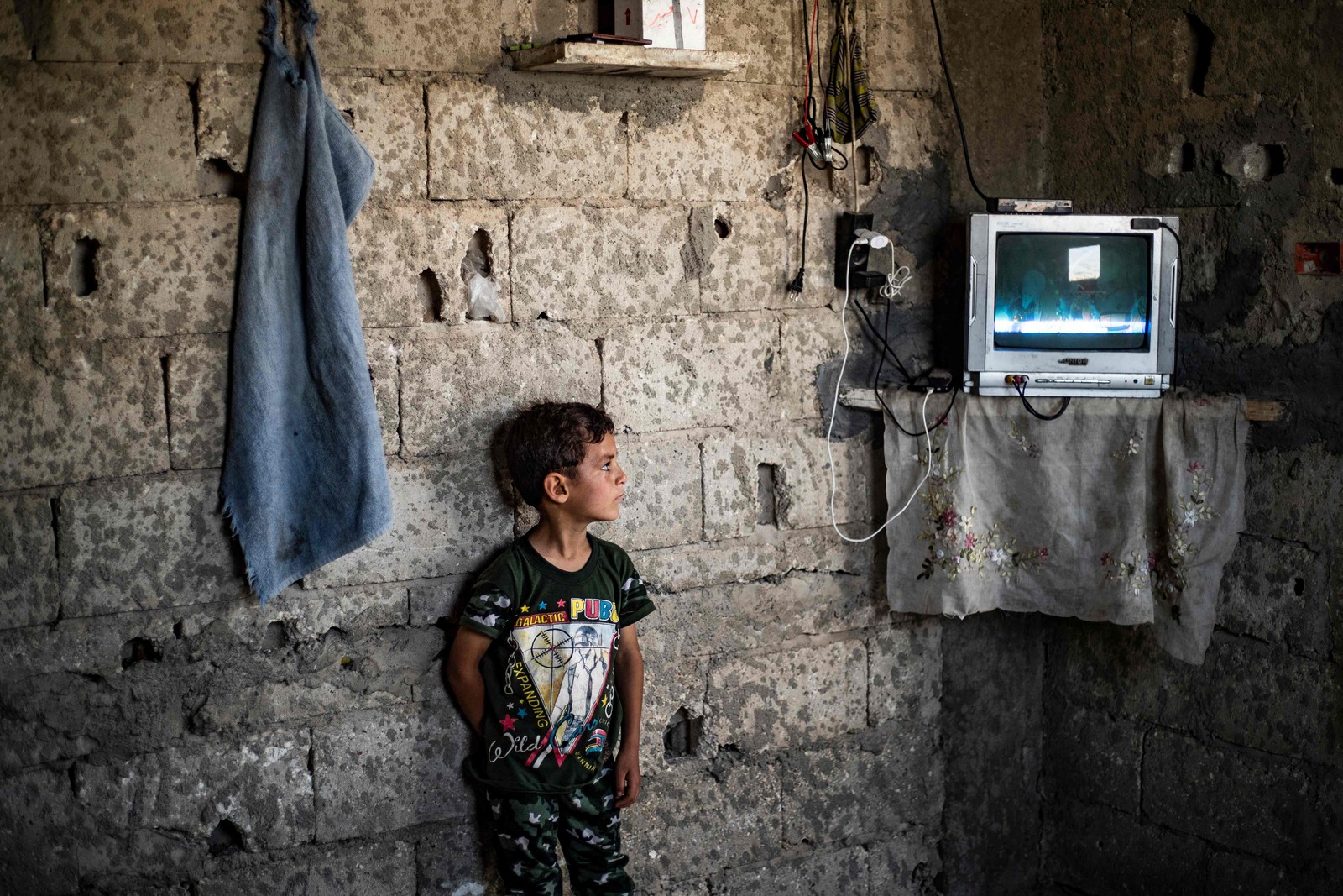 Menino sírio observa dentro do prédio danificado onde mora na cidade de Raqa, no norte do país. Ele foi deslocado pela guerra civil sua família de Deir Ez-Zor — Foto: DELIL SOULEIMAN / AFP