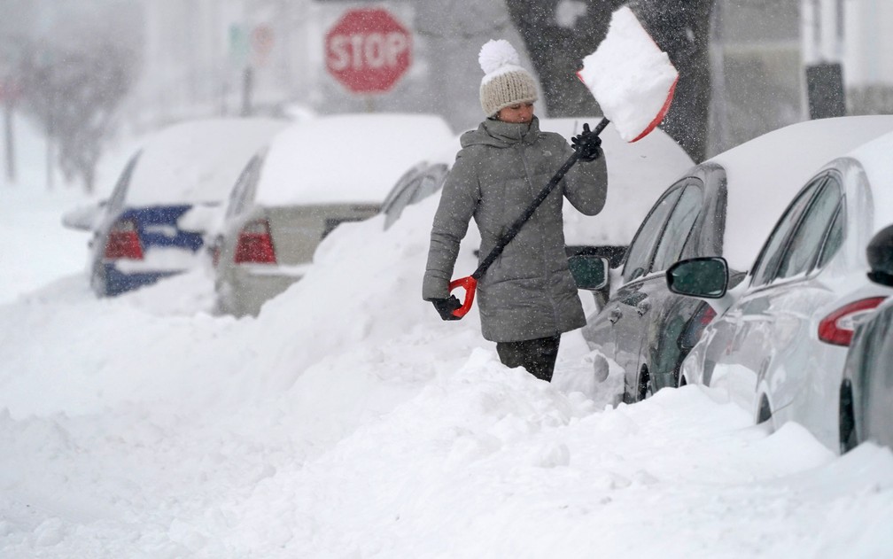 Mulher retira excesso de neve do lugar onde seu carro está estacionado, em Manchester, New Hampshire, na quinta-feira (17) — Foto: AP Photo/Charles Krupa