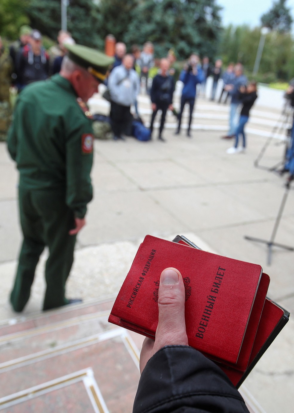 Oficial do exército russo segura carteiras de identidade militar enquanto reservistas se reúnem em um ponto de encontro na cidade de Volzhsky, na Rússia — Foto: Reuters/Stringer
