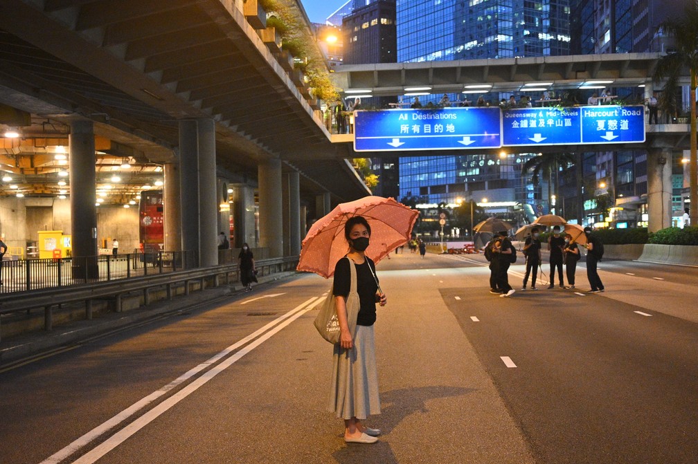 Uma mulher usando uma máscara e segurando um guarda-chuva para no meio da rua nesta sexta-feira (4), no momento em que o trânsito parou por causa dos protestos em Hong Kong. — Foto: Philip Fong/AFP