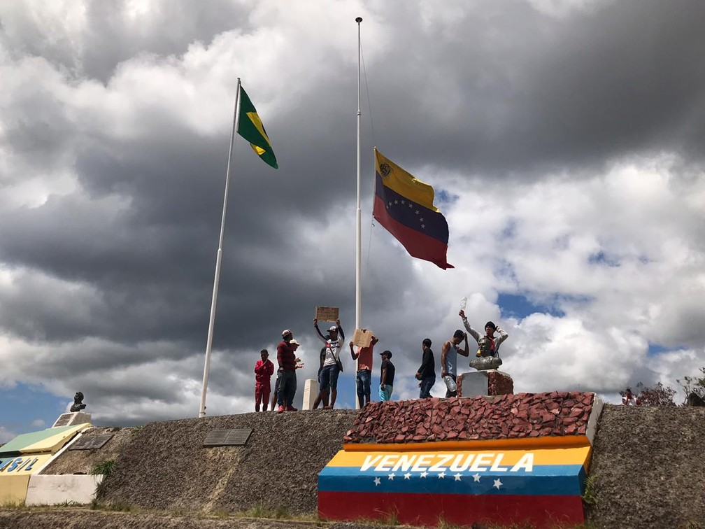 Grupo de venezuelanos baixa bandeira hasteada na linha de fronteira — Foto: Alan Chaves/G1 RR