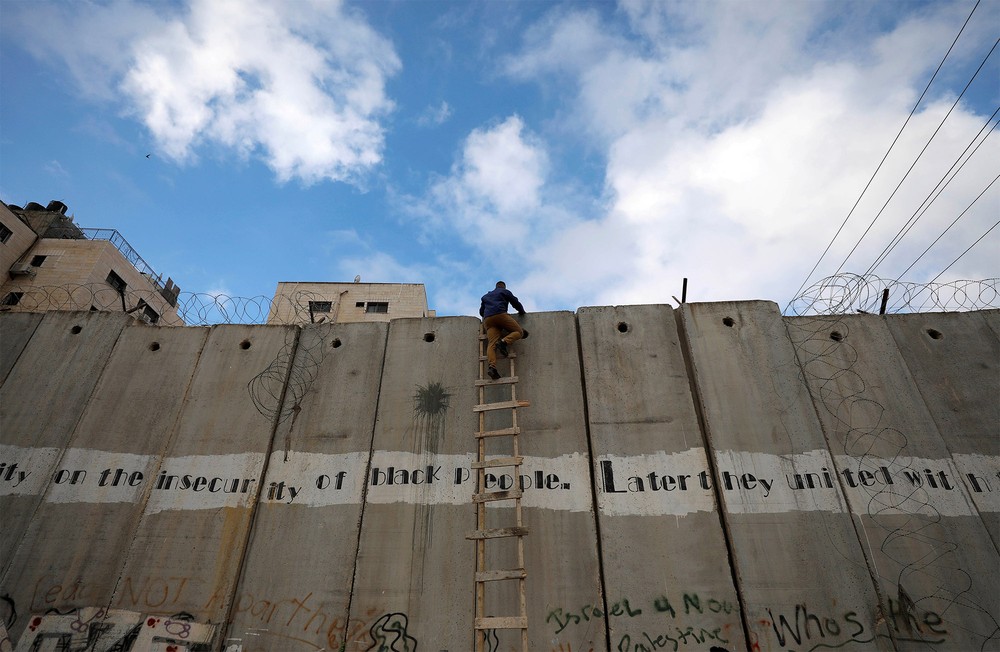 Um palestino usa uma escada para pular um muro israelense perto de Ramallah, Cisjordânia, e tentar chegar às primeiras orações de sexta-feira no mês sagrado islâmico do Ramadã na mesquita Al-Aqsa, em Jerusalém — Foto: Mohamad Torokman/Reuters