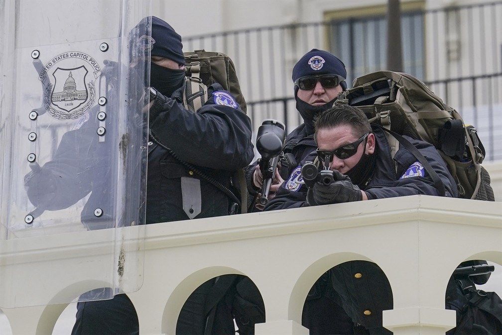 Policiais fazem guarda observando manifestantes pró-Trump do lado de fora do Capitólio dos EUA durante invasão — Foto: John Minchillo/AP