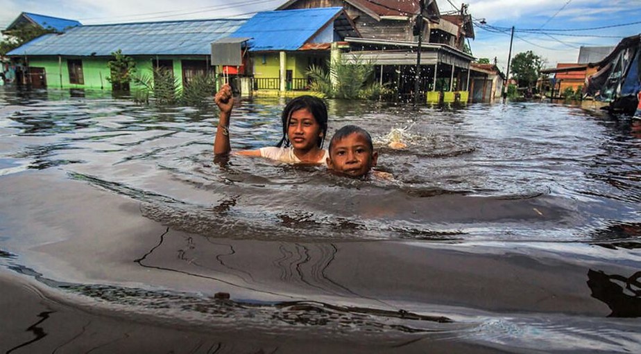 Crianças atravessam um 'mar' em plena rua da Indonésia afetada por enchentes.