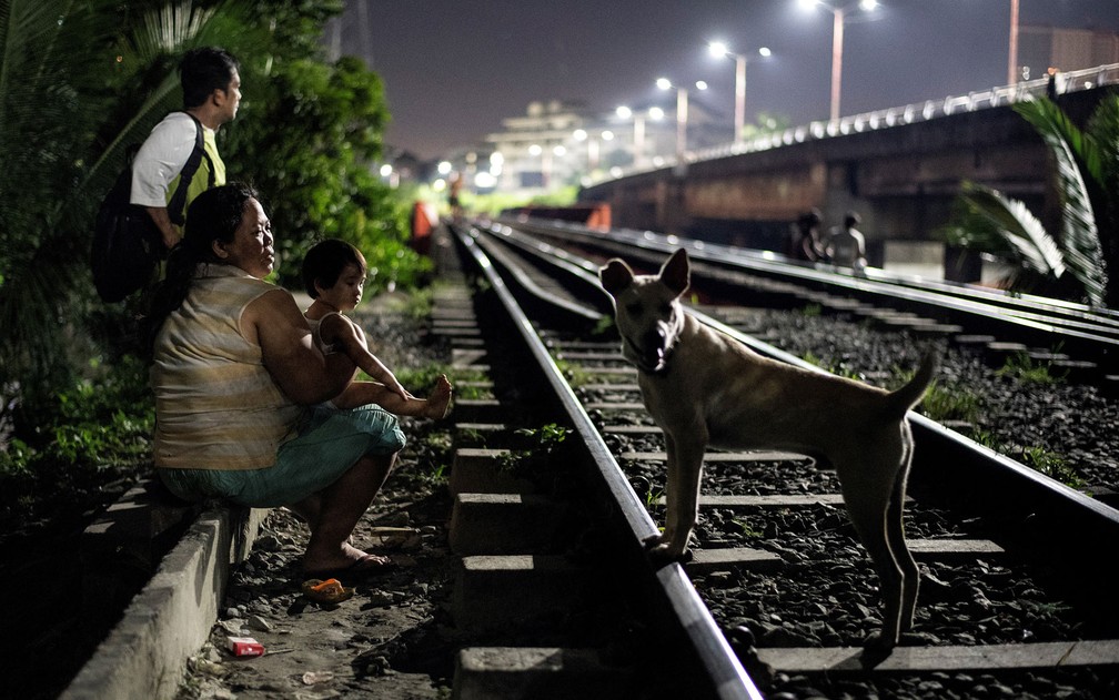 Foto de 19 de outubro mostra mãe com criança sentadas ao lado de linha de trem de Manila, aguardando para pegar um carrinho — Foto: Noel Celis/AFP
