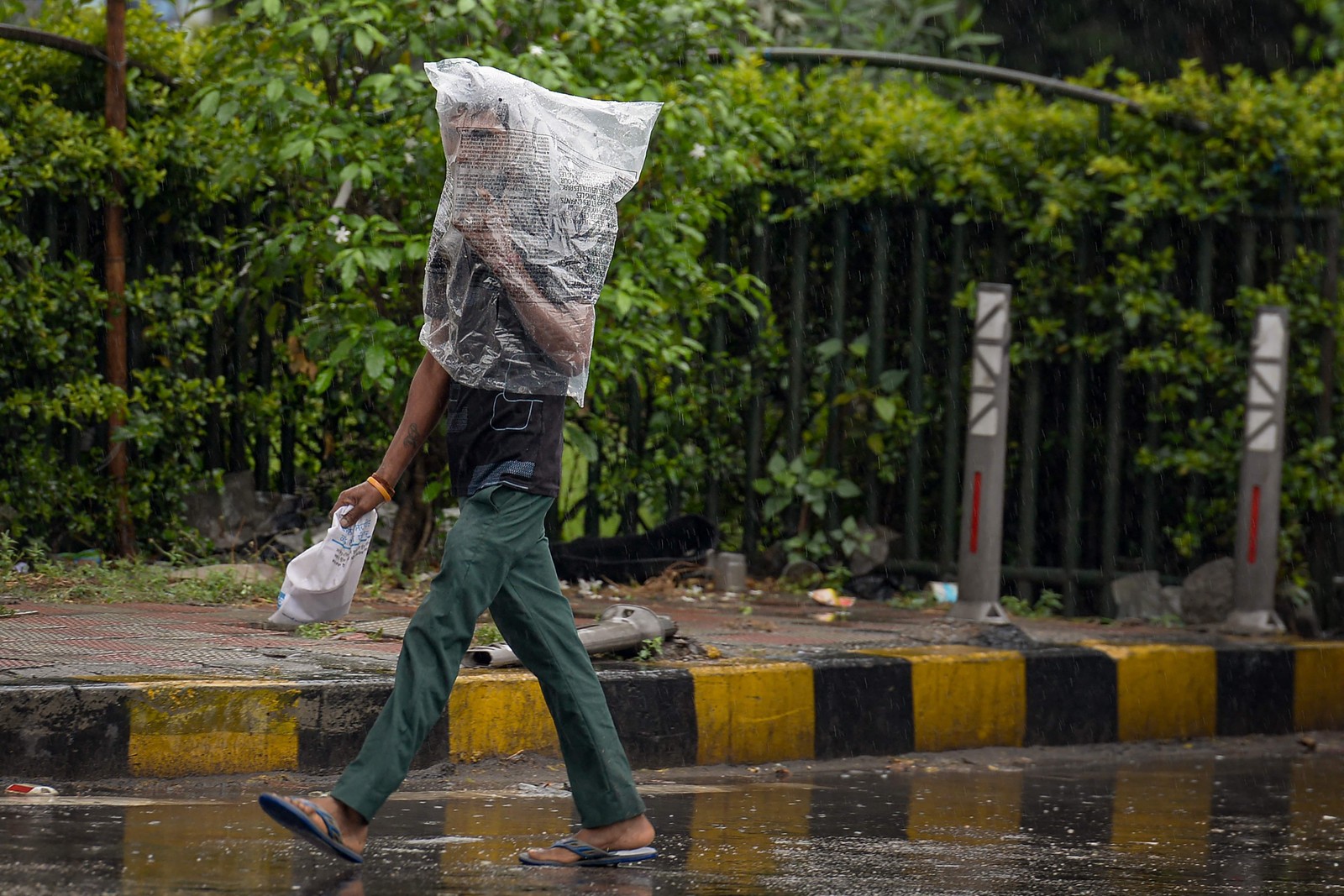 Pedestre usa um saco plástico para se cobrir durante uma chuva torrencial em Jalandhar, Índia — Foto: SHAMMI MEHRA/AFP