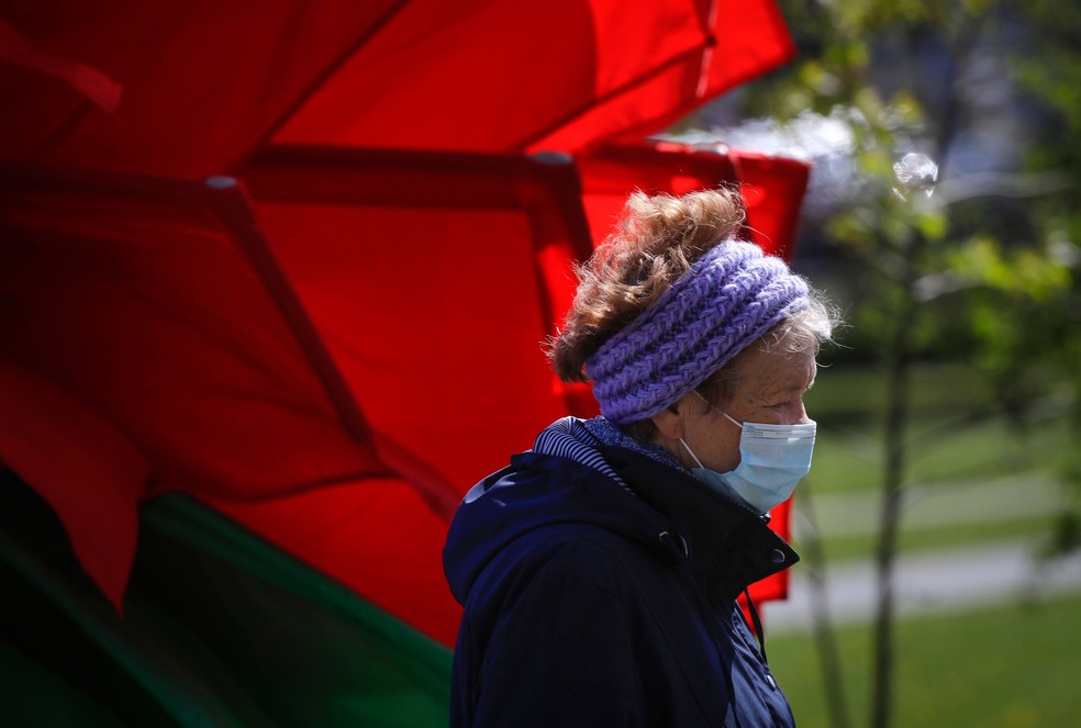 Uma mulher com máscara passa por bandeiras nas cores vermelho e verde enquanto a cidade de Minsk, em Belarus, se prepara para o desfile militar do Dia da Vitória que ocorrerá no sábado (9)  — Foto: Sergei Grits/AP