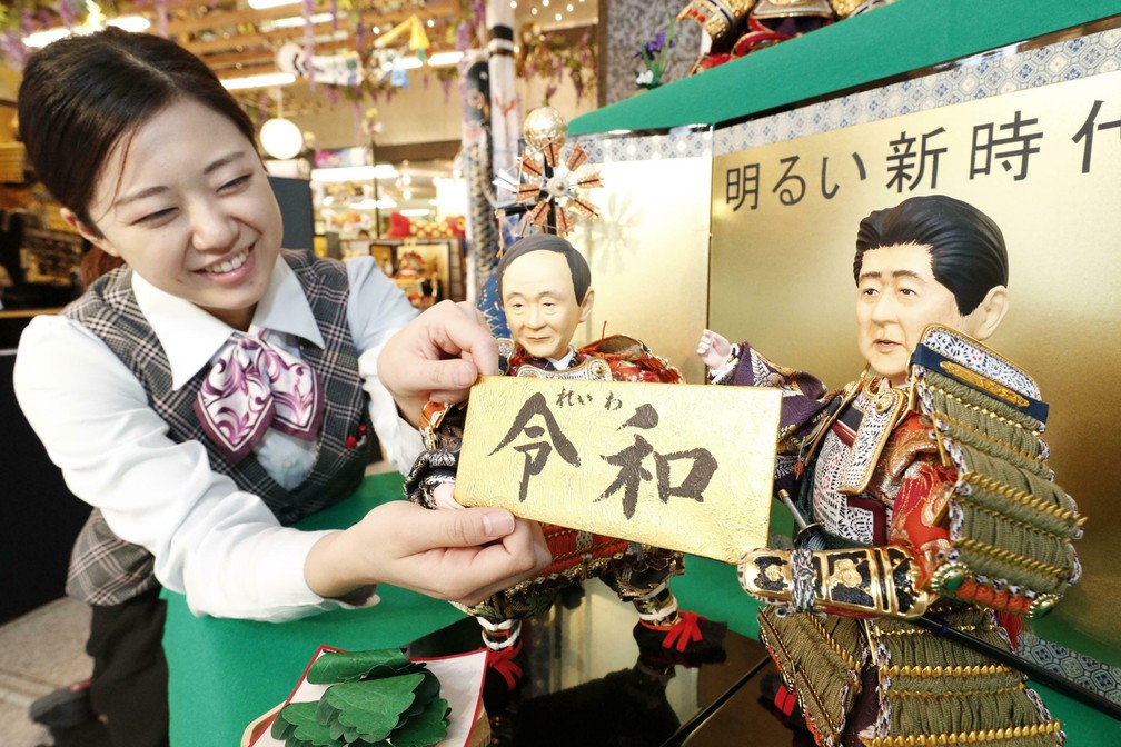 Vendedora segura placa com o nome da nova era imperial japonesa, Reiwa, em uma empresa de bonecas japonesa em Tóquio, no dia do anúncio, em 1º de abril. — Foto: Satoru Yonemaru/Kyodo News via AP