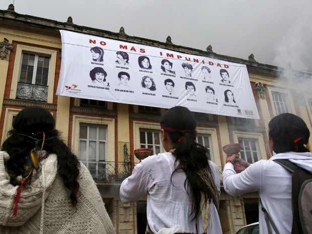 Mulheres queimam incensos em frente a um painel com fotos de mortos e desaparecidos no cerco ao Palácio da Justiça de Bogotá, em cerimônia na sexta (6) (Foto: Reuters/John Vizcaino)