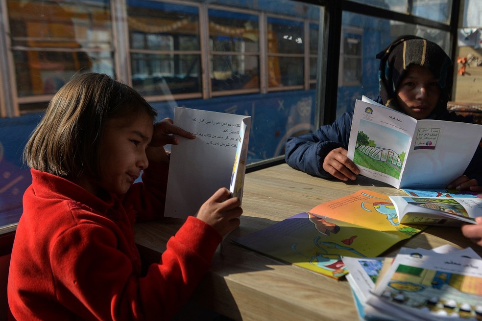 Crianças leem livros em uma biblioteca móvel de Cabul que abriu suas portas pela primeira vez desde a volta do Talibã ao poder no Afeganistão — Foto: Ahmad Sahel Arman/AFP