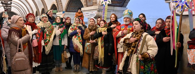 Moradores em trajes tradicionais cantam canções de Natal dentro de uma estação de metrô em Kyiv — Foto: SERGIO CHUZAVKOV/AFP