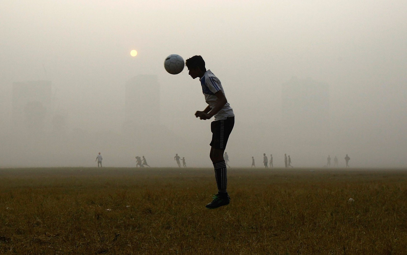 Um homem pula para cabecear durante treino de futebol em meio a neblina em um parque público de Kolkata, na Índia