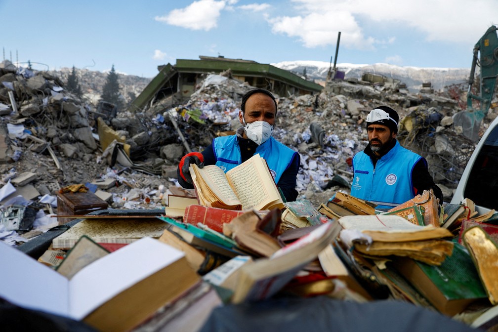 Pessoas retiram manualmente cópias do Alcorão e do Evangelho do meio dos escombros em Kahramanmaras, na Turquia — Foto: Suhaib Salem/REUTERS