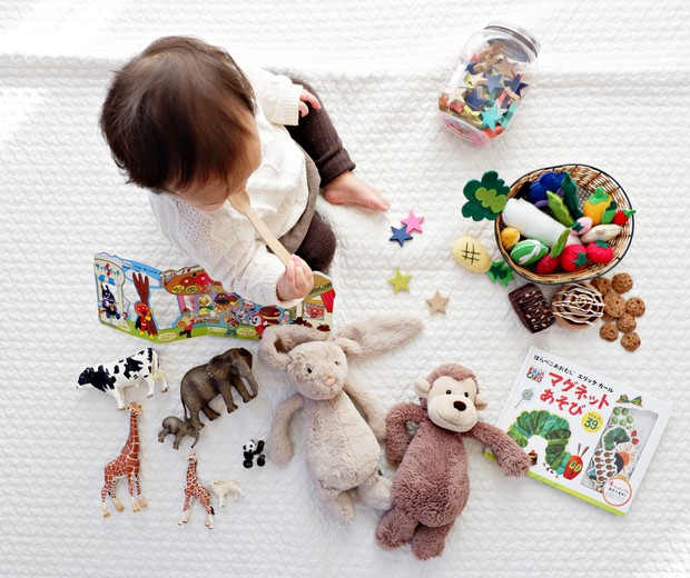 Bebê menino brincando de boneca, carrinho, ursinho de pelúcia (Foto: Unsplash)