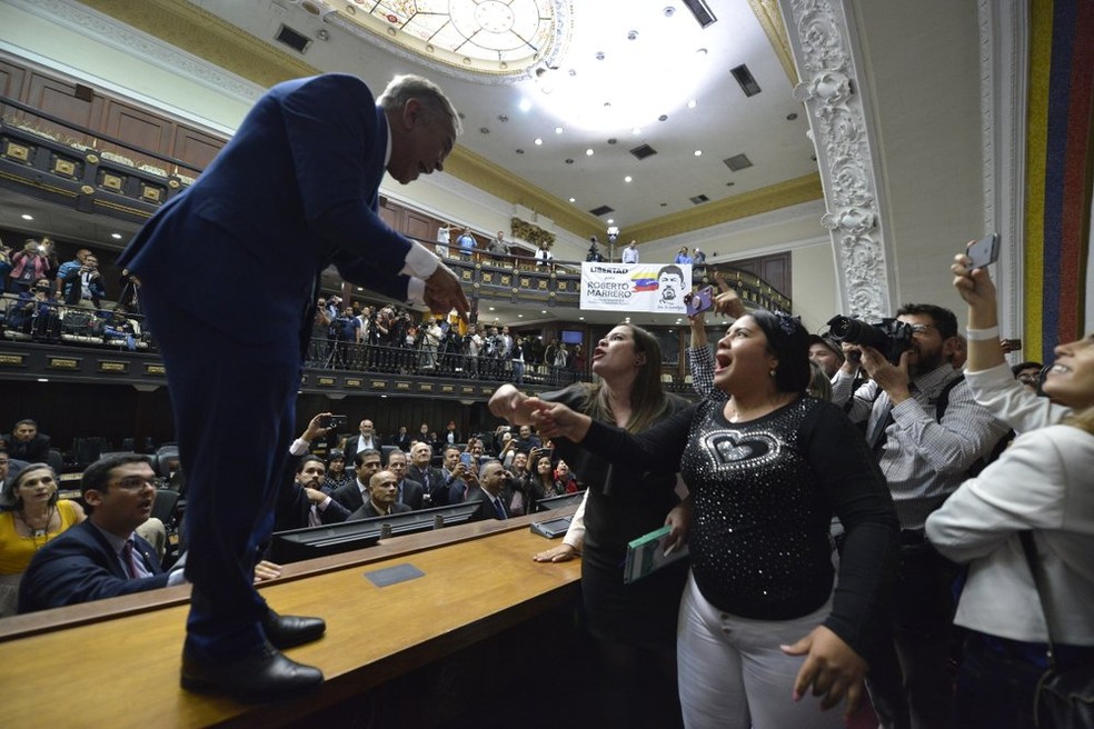 O deputado da oposição, William Barrientos, pró Guaidó, sobe em uma mesa para discutir com os legisladores após conseguir entrar na Assembleia Legislativa, neste domingo (5). — Foto: AP Photo/Matias Delacroix