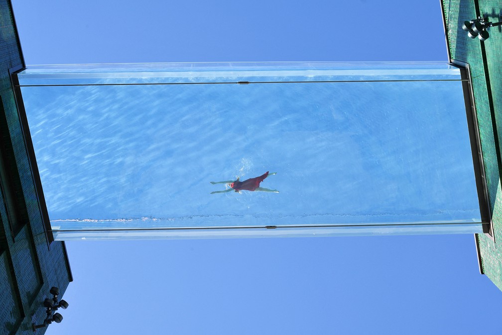 Uma modelo nada em uma piscina de acrílico transparente fixada entre dois blocos de apartamentos em Embassy Gardens, em Londres.  — Foto: Justin Tallis/AFP
