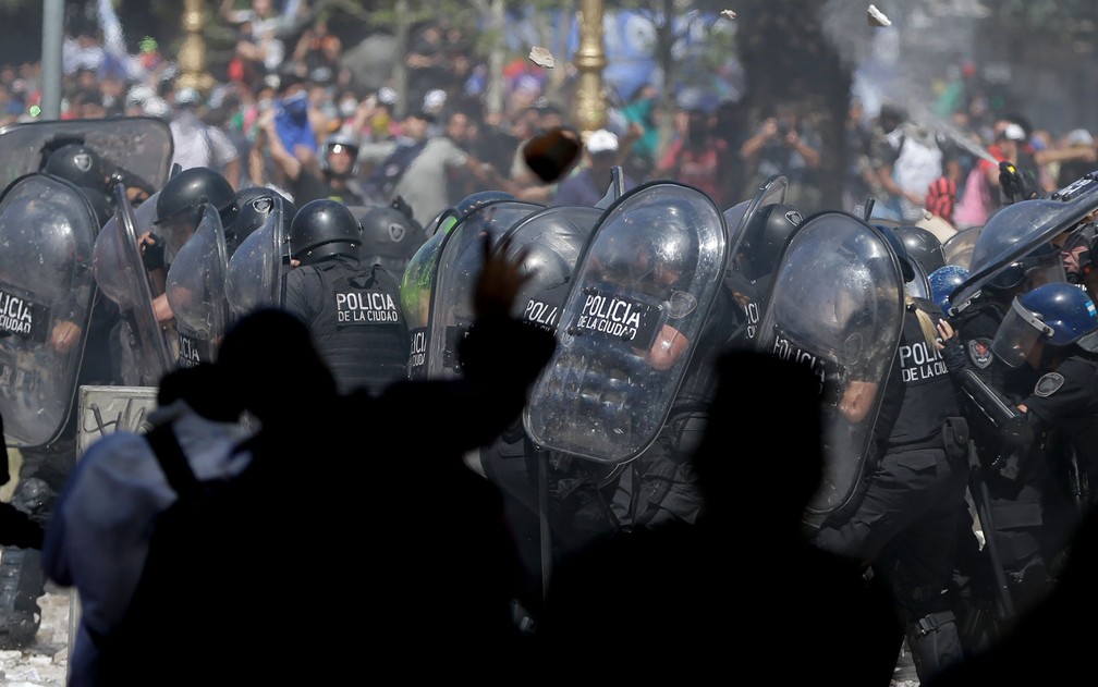 Policiais se protegem de pedras atiradas por manifestantes durante confrontos em frente ao Congresso Nacional em votação pela reforma da previdência, em Buenos Aires, na Argentina, na segunda-feira (18) (Foto: AP Photo/Natacha Pisarenko)