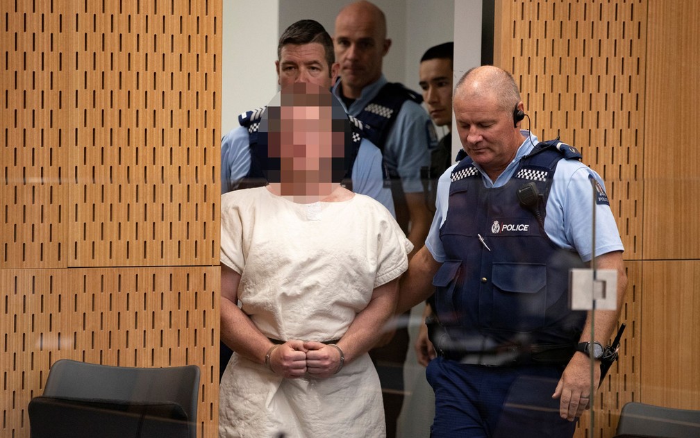Brenton Tarrant é acompanhado por policiais durante sua apresentação à corte do Distrito de Christchurch, na Nova Zelândia, no sábado (16)  — Foto: Mark Mitchell/New Zealand Herald/Pool