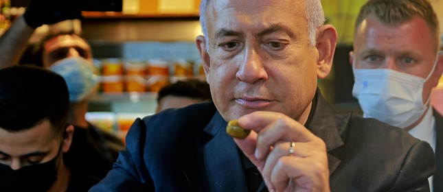 O primeiro-ministro israelense Benjamin Netanyahu come uma azeitona de uma barraca enquanto visita o mercado Mahane Yehuda em Jerusalém,  enquanto faz campanha um dia antes da quarta eleição nacional em dois anos