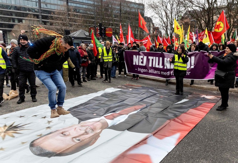 Manifestante salta sobre faixa estampada com o rosto de Erdogan em protesto em Estocolmo