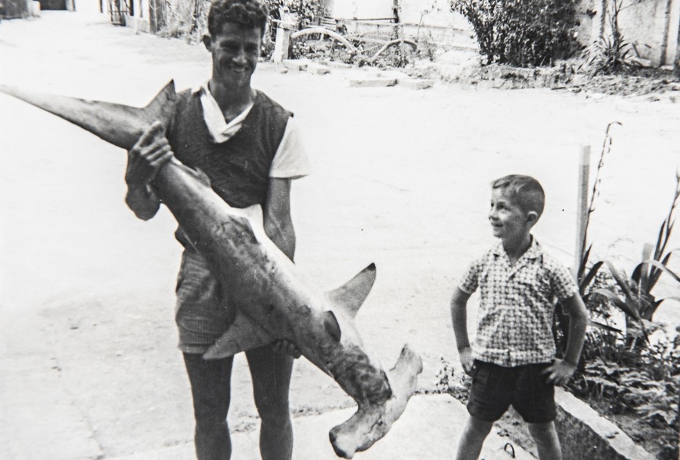 Cláudio Fischer, morador da região, ao lado de um pescador segurando um tubarão martelo; registro da década de 1960 — Foto: Arquivo histórico de Balneário Camboriú/ Divulgação
