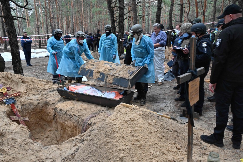 Equipes forenses retiram um caixão de uma cova coletiva nos arredores de Izium