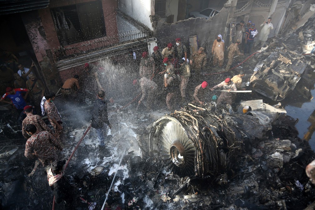 22 de maio - Equipes de resgate e moradores locais procuram sobreviventes nos destroços de um avião que caiu com quase 100 pessoas a bordo em uma área residencial de Karachi, no Paquistão  — Foto: Fareed Khan/AP