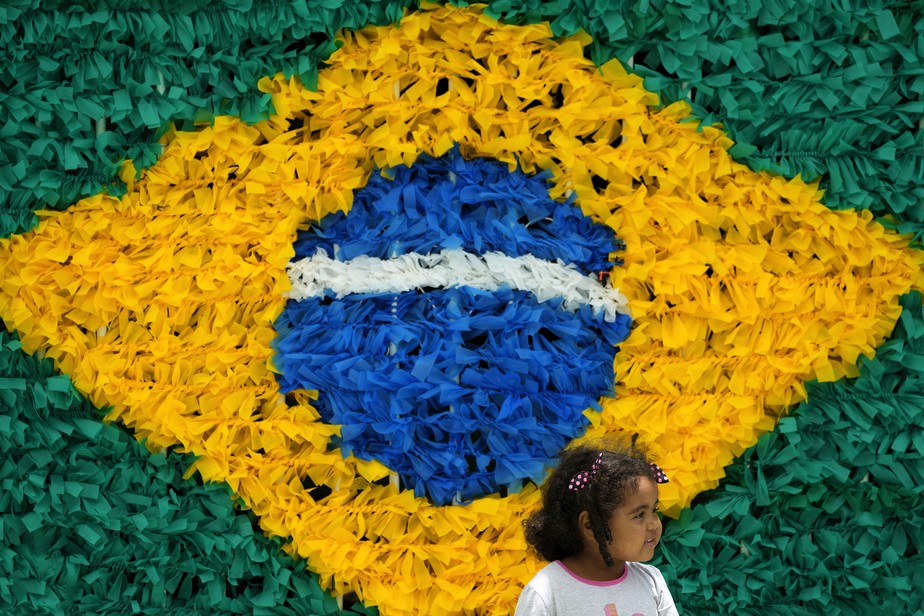 Em Brasília, menina em frente a um painel decorado com bandeira do Brasil feita com laços de plástico