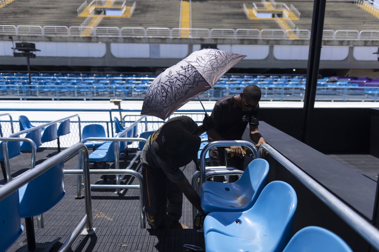 Sombrinha protege trabalhador do sol enquanto faz ajustes nas cadeiras da Sapucaí — Foto: Márcia Foletto/Agência O Globo