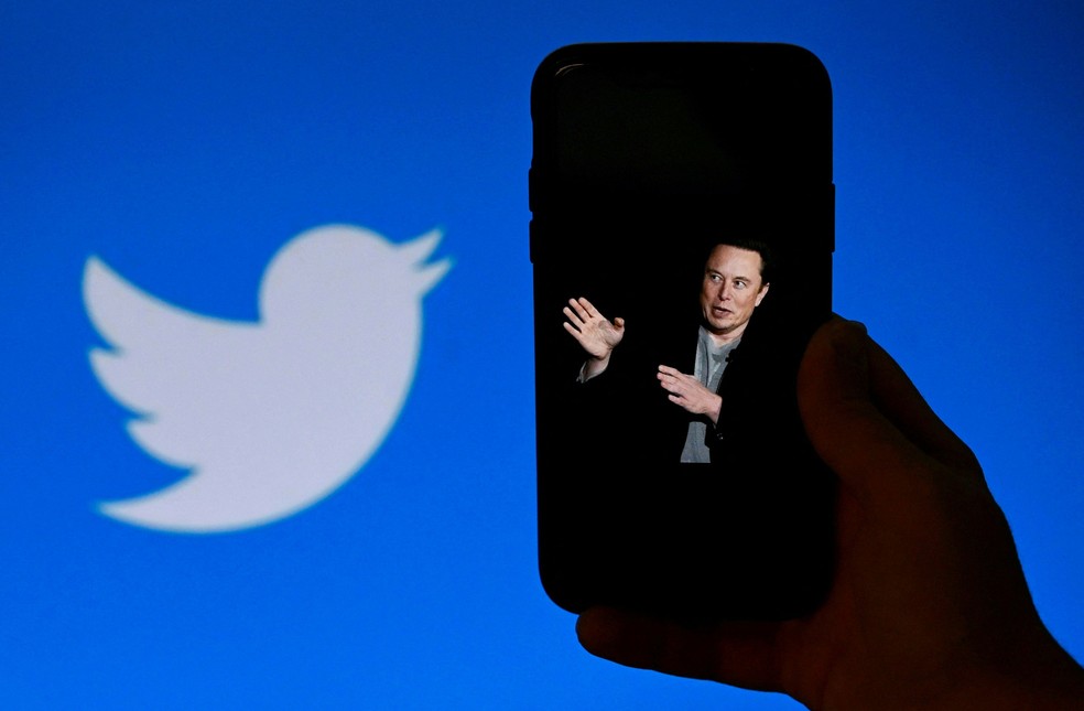 Tela de celular exibe foto de Elon Musk com a logo do Twitter ao fundo — Foto: Olivier Douliery/AFP