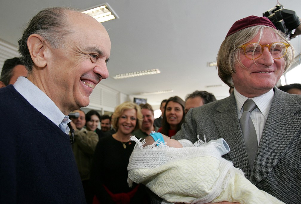 O então candidato à Prefeitura de São Paulo pelo PSDB, José Serra, posa ao lado do rabino Henry Sobel, que segura um bebê, durante visita ao ambulatório comunitário do Hospital Albert Einstein, na favela Paraisópolis, no Morumbi, Zona Sul da capital, em julho de 2004 — Foto: Nilton Fukuda/Estadão Conteúdo