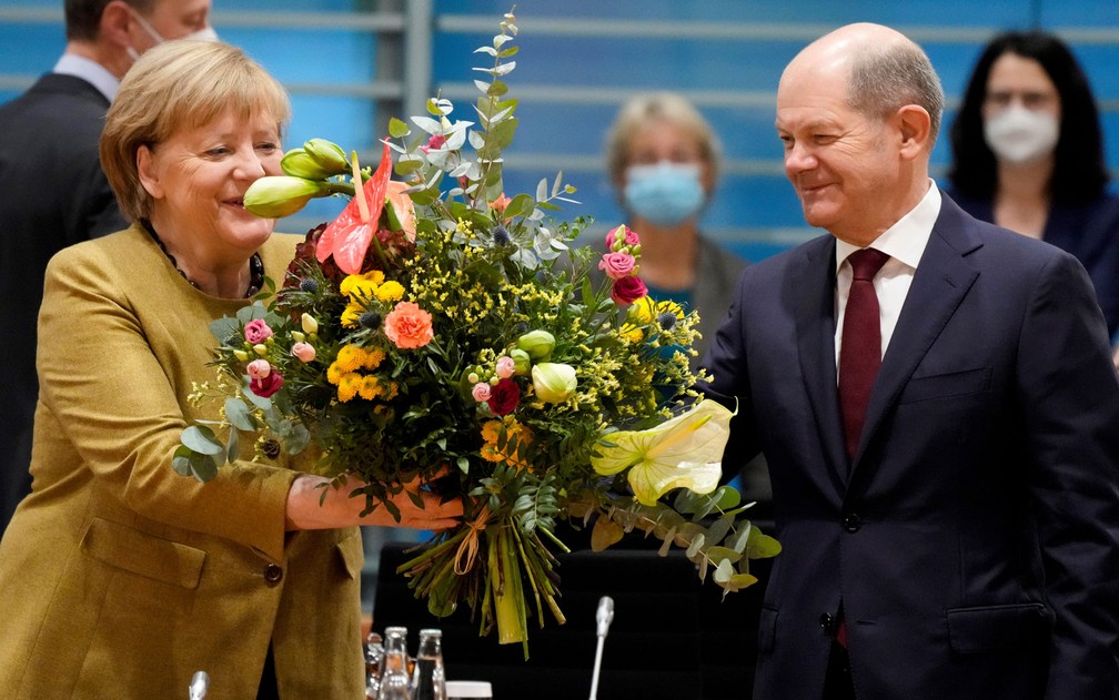 A primeira-ministra da Alemanha, Angela Merkel, recebe flores de seu futuro substituto, Olaf Scholz, em Berlim, em foto de 24 de novembro — Foto: Markus Schreiber/Pool via Reuters