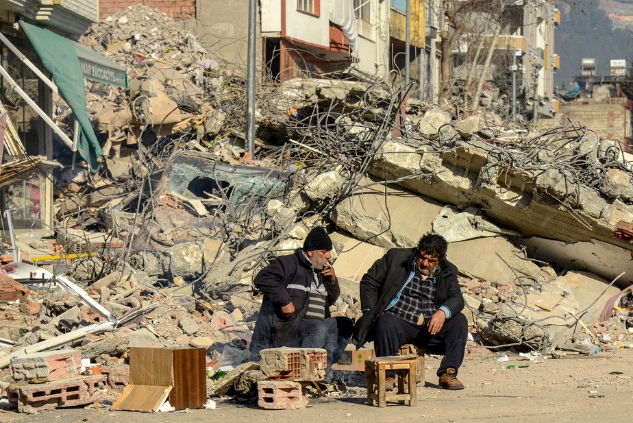 Parentes das vítimas sentam-se ao lado dos escombros de um prédio que desabou em Adiyaman após o terremoto que atingiu o Sudeste da Turquia