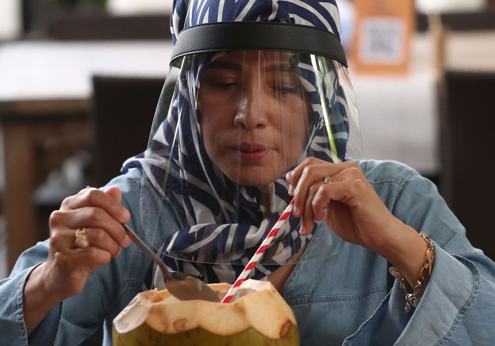 Mulher com protetor facial come um coco fresco em um restaurante de frutos do mar nos arredores de Jacarta, na Indonésia, nesta quarta-feira (10)  — Foto: Tatan Syuflana/AP 